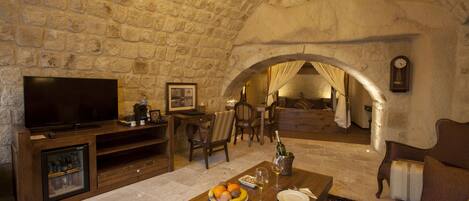 A stone-walled room with a television, wooden furniture, a dining table with plates and glasses, and a clock on the wall.