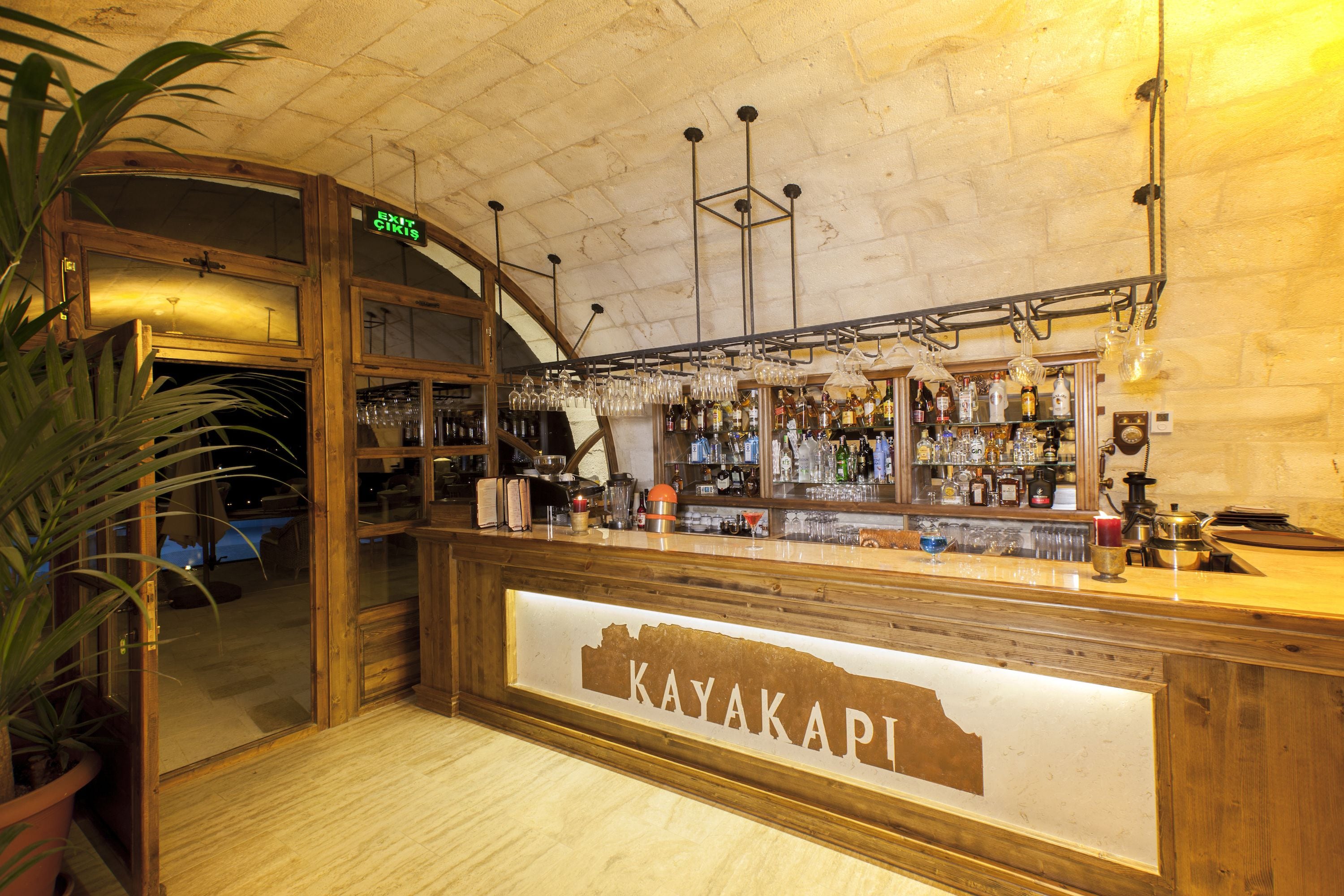 A bar area with a wooden counter, shelves of bottles, and glasses.