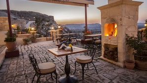 A restaurant patio with stone flooring, outdoor seating, and a stone fireplace. - Kayakapi Premium Caves - Cappadocia (Ürgüp)