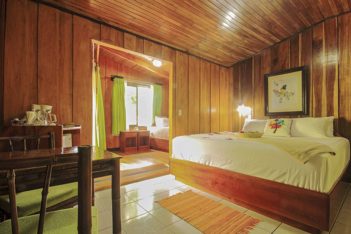 A wooden-paneled room with a bed, a dining table with chairs, and a small kitchen area.