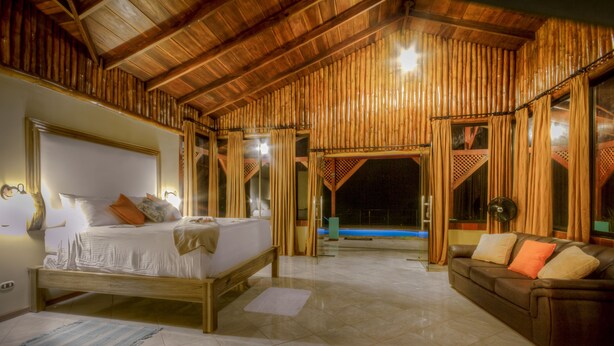 A spacious room with a large bed, a sofa, and a view of a swimming pool. - Arenal Waterfall Lodge (La Fortuna)