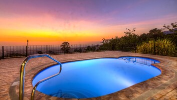 Una piscina con vista a la puesta de sol y luces distantes de la ciudad.