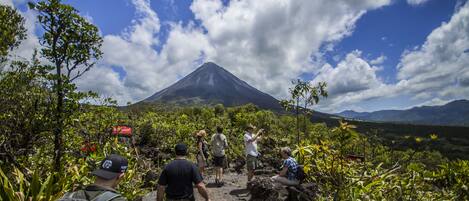 A group of people hiking on a rocky trail with a volcano in the background.