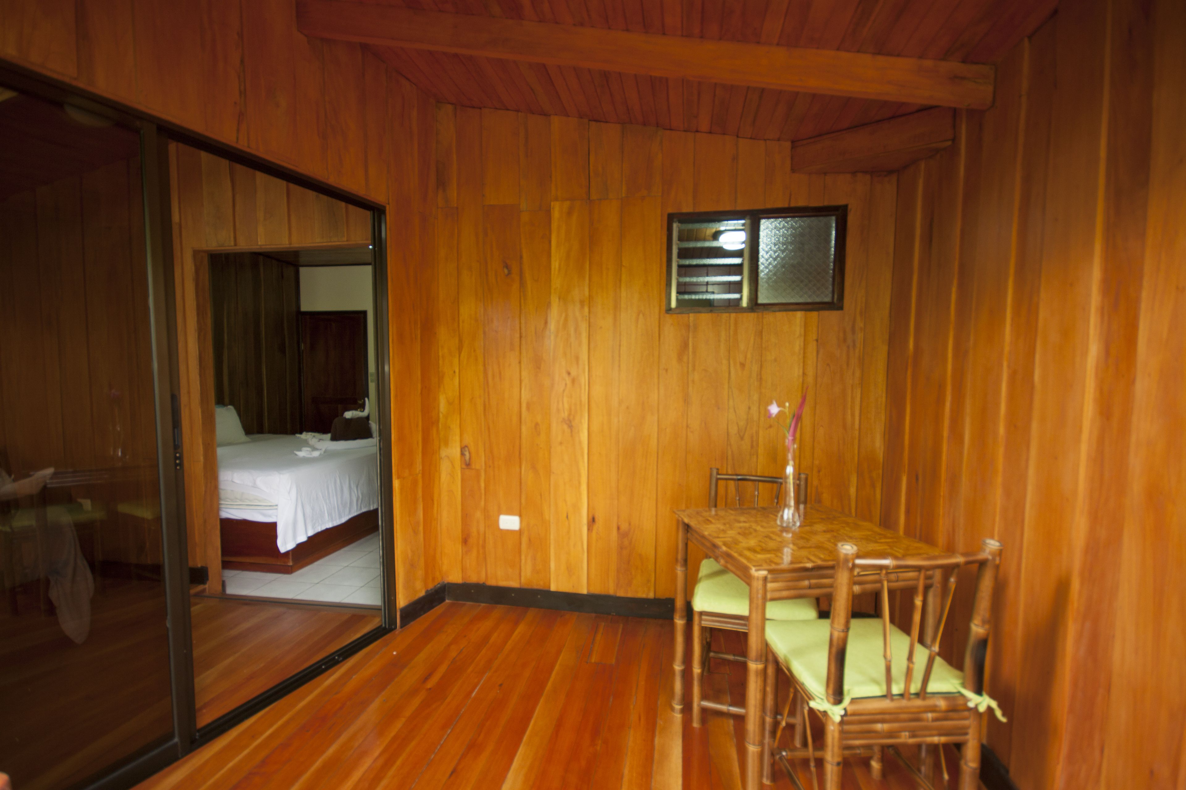Ein Zimmer mit Holzwänden, einem Bett, einem Esstisch mit Stühlen und einer Schiebetür aus Glas zu einem anderen Raum.