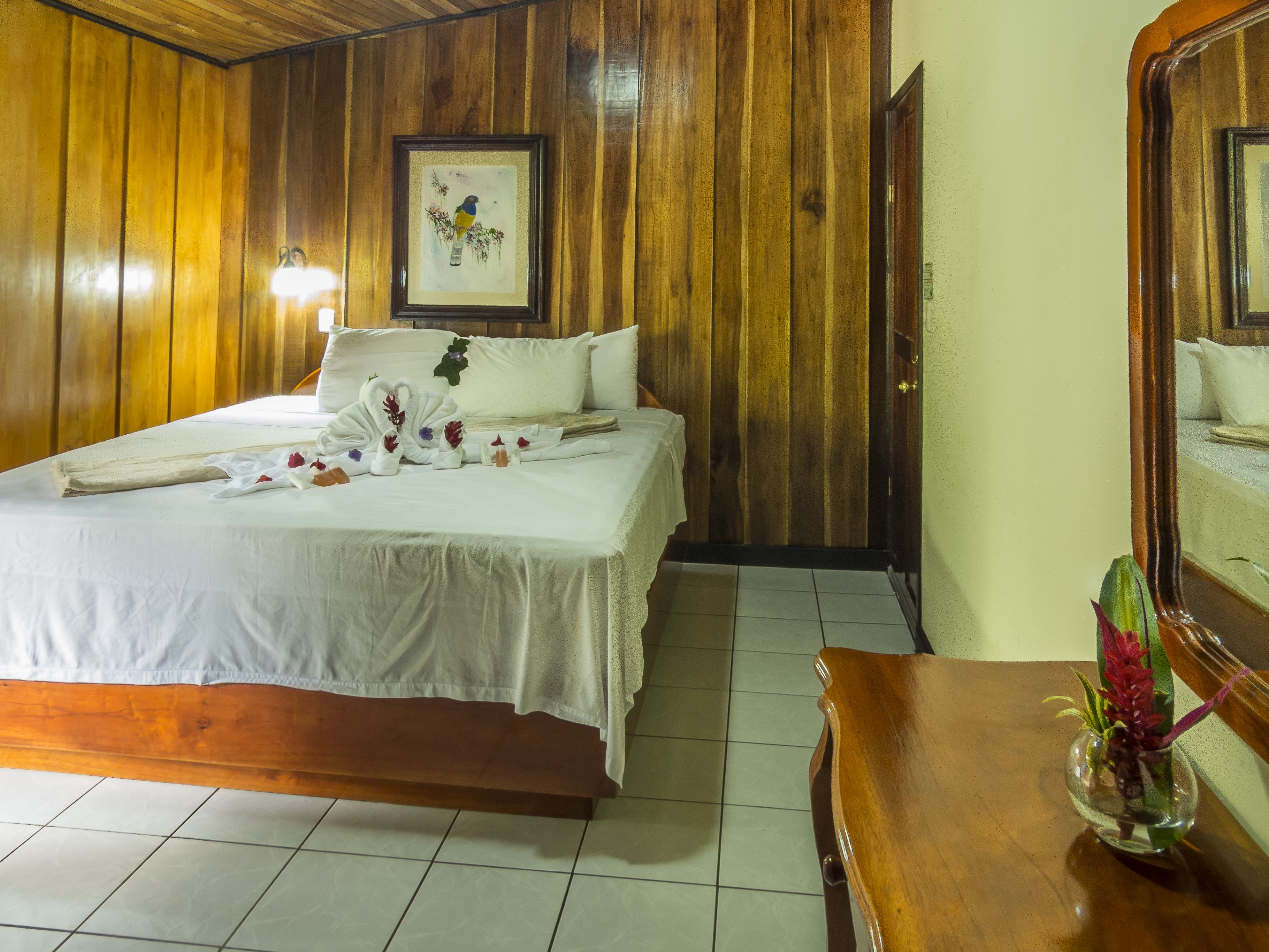 A wooden-paneled room with a bed, a framed picture on the wall, and a small table with a vase.