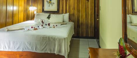 A wooden-paneled room with a bed, a framed picture on the wall, and a small table with a vase.