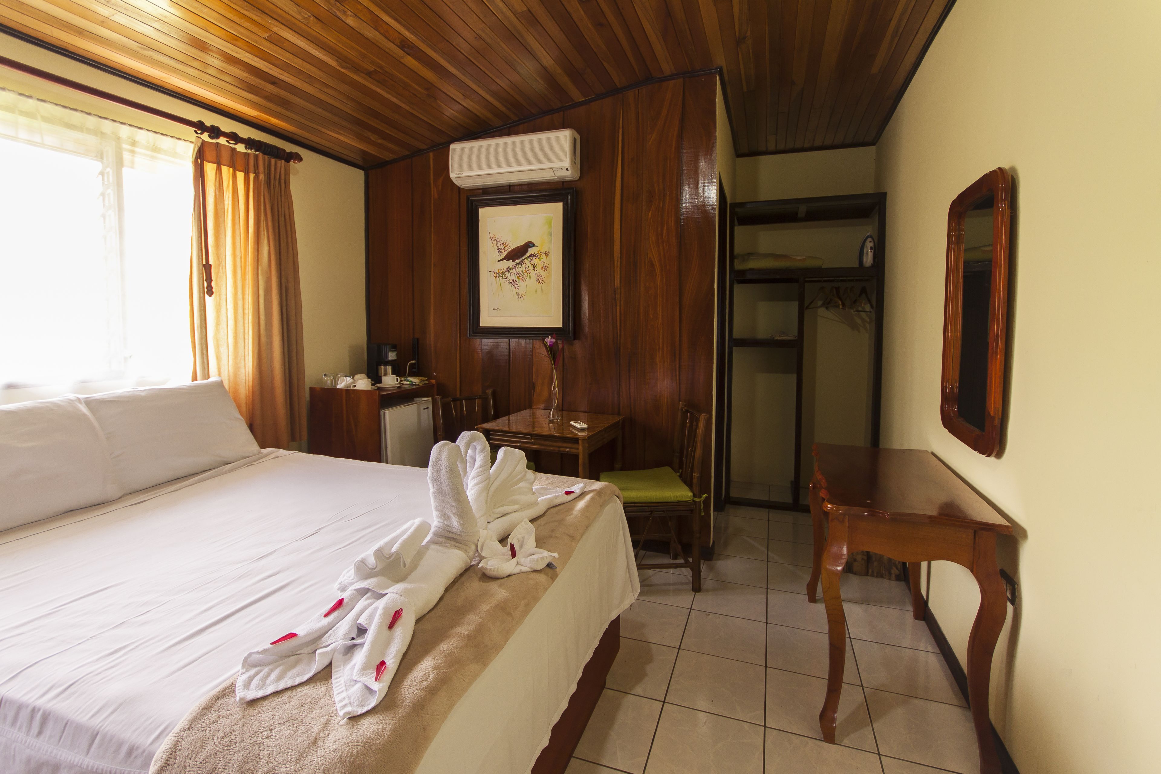 Ein Hotelzimmer mit Bett, Schreibtisch, Stuhl, Spiegel und einem gerahmten Bild an der Wand.