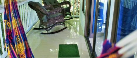 Une véranda couverte avec des fauteuils à bascule en osier et un tapis vert sur le sol.