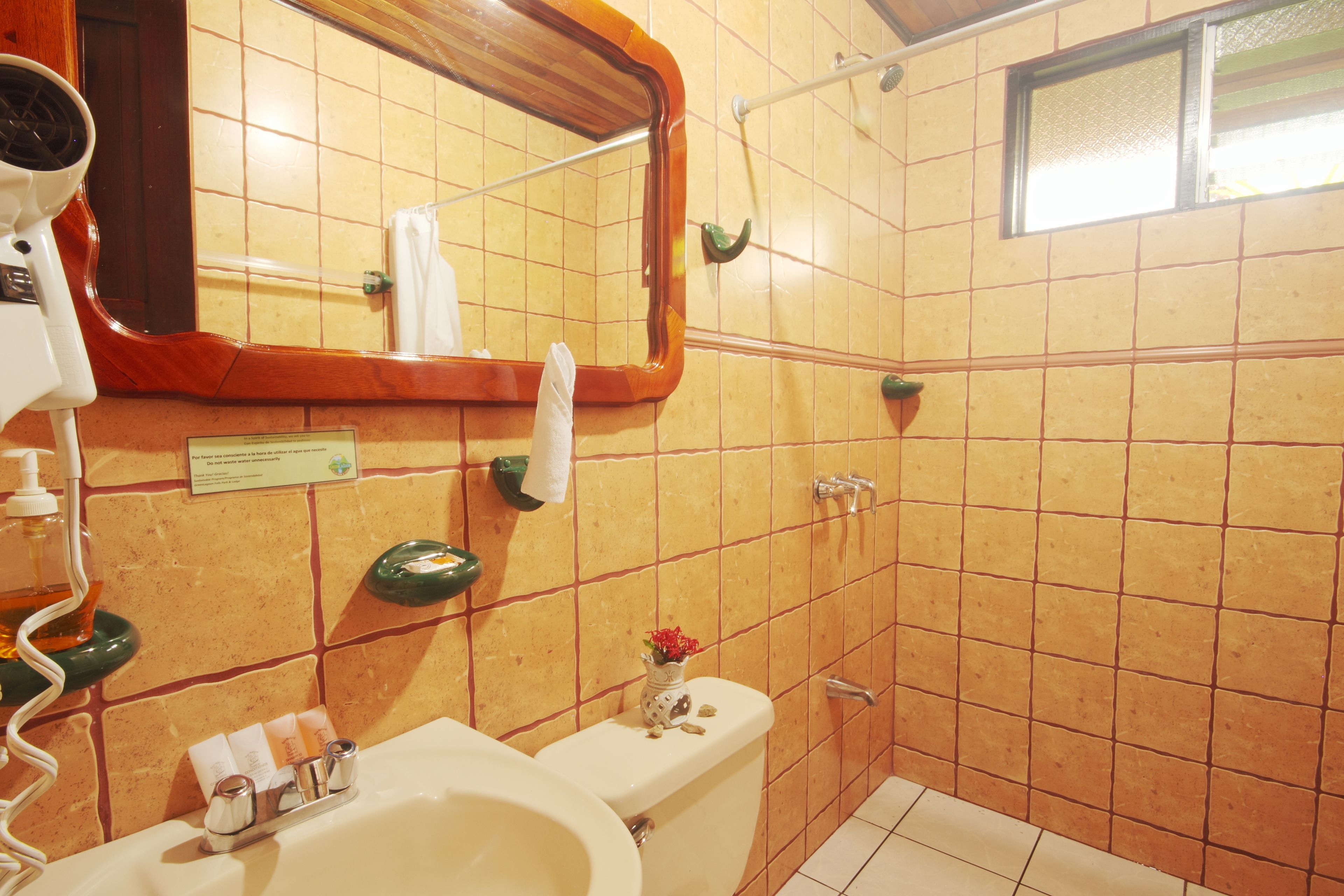 A bathroom with a sink, mirror, and toilet. There is a towel rack and a small vase with flowers on the toilet.