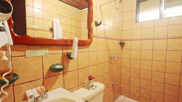 A bathroom with a sink, mirror, and toilet. There is a towel rack and a small vase with flowers on the toilet.