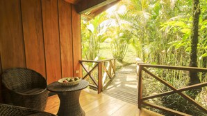 A wooden deck with wicker furniture and a view of lush greenery. - Arenal Waterfall Lodge (La Fortuna)