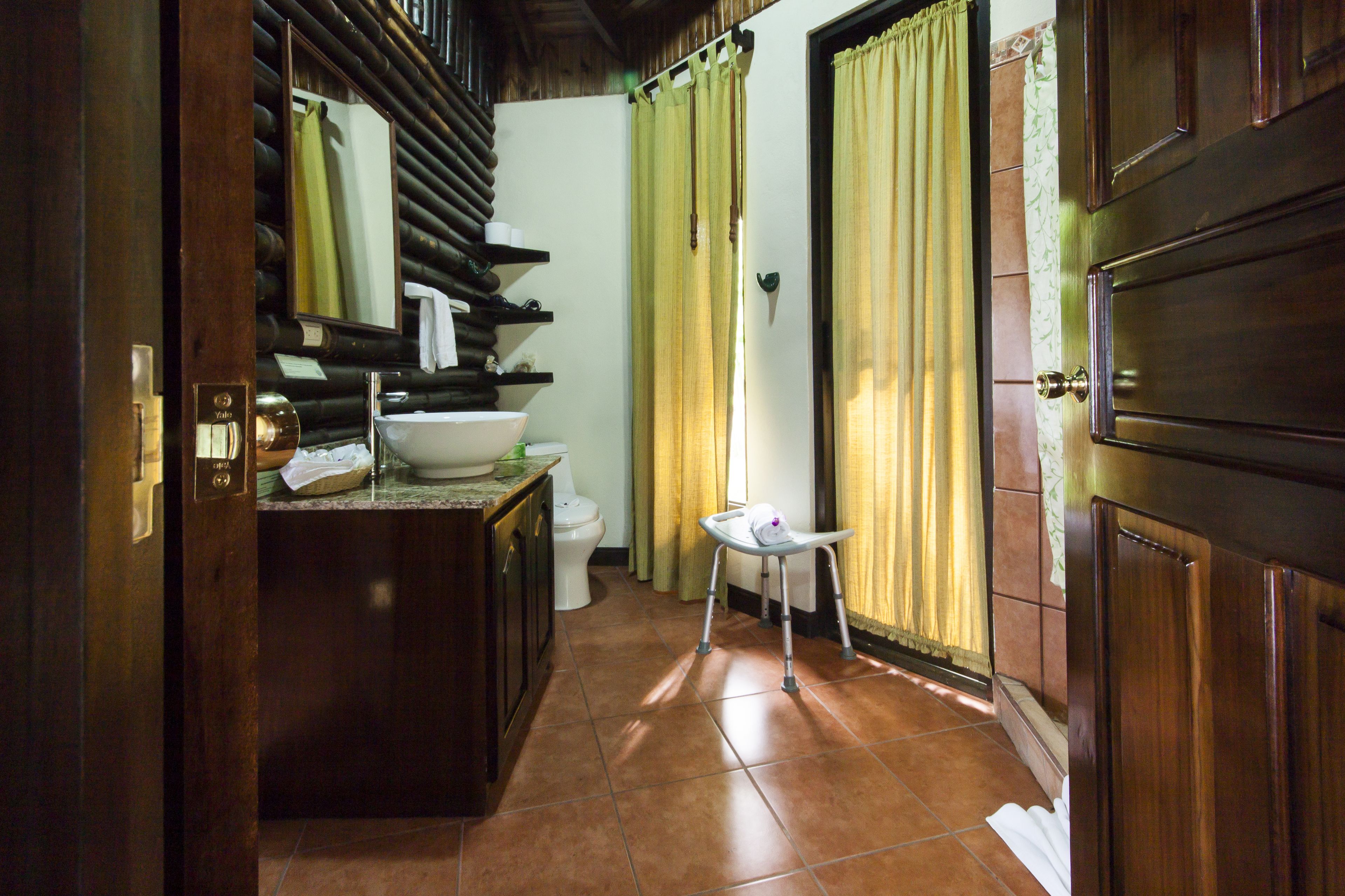 A bathroom with a wooden vanity, a sink, and a toilet. There is a small stool near the window.
