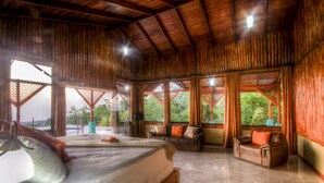 A spacious room with a large bed, two sofas, and a view of greenery outside. - Arenal Waterfall Lodge (La Fortuna)