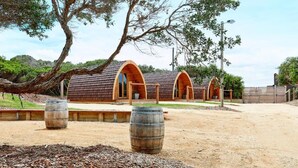 Una hilera de cabañas de madera con puertas en arco, rodeadas por un camino de tierra y árboles.