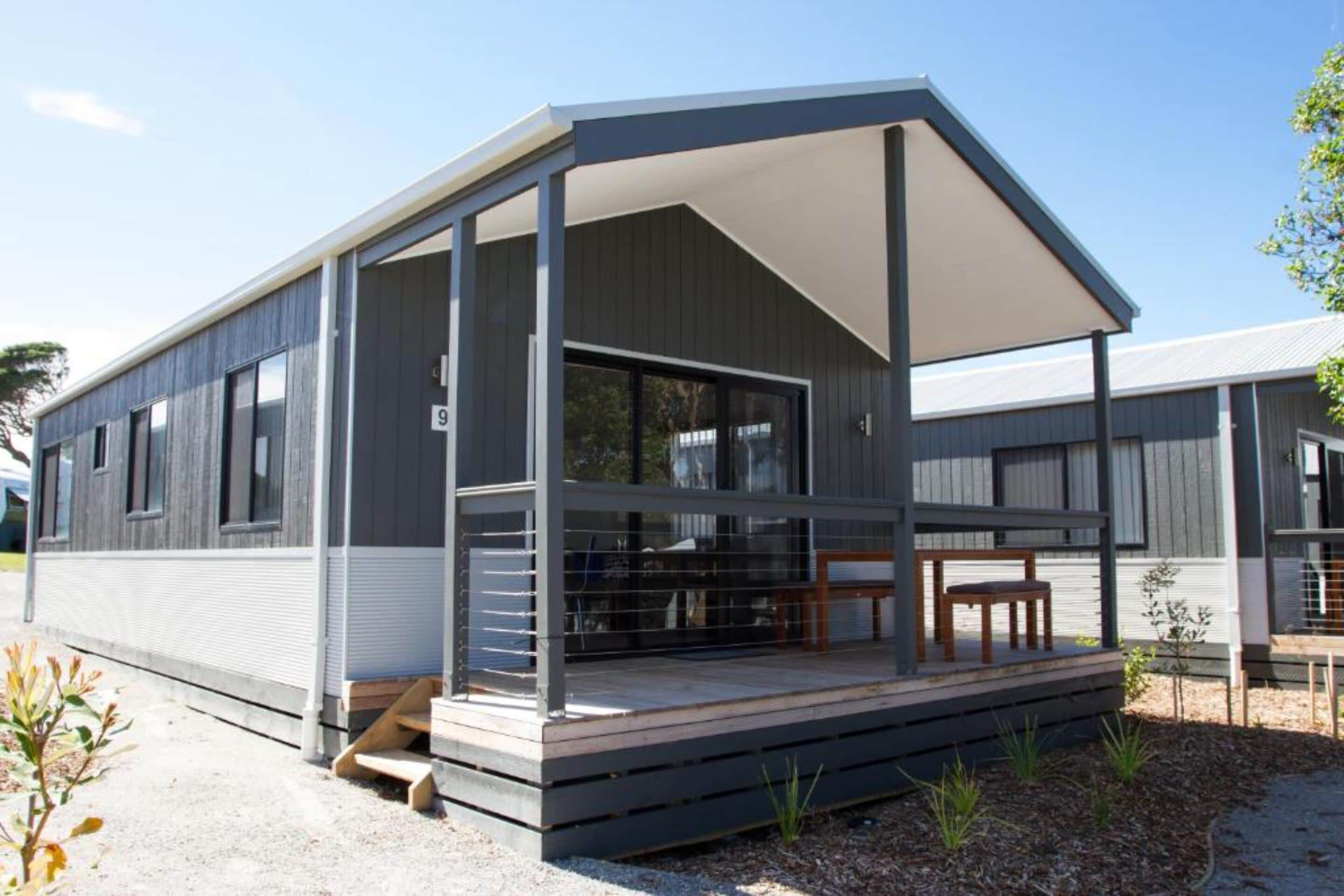 A modern, single-story mobile home with a covered porch, large windows, and a small deck area.