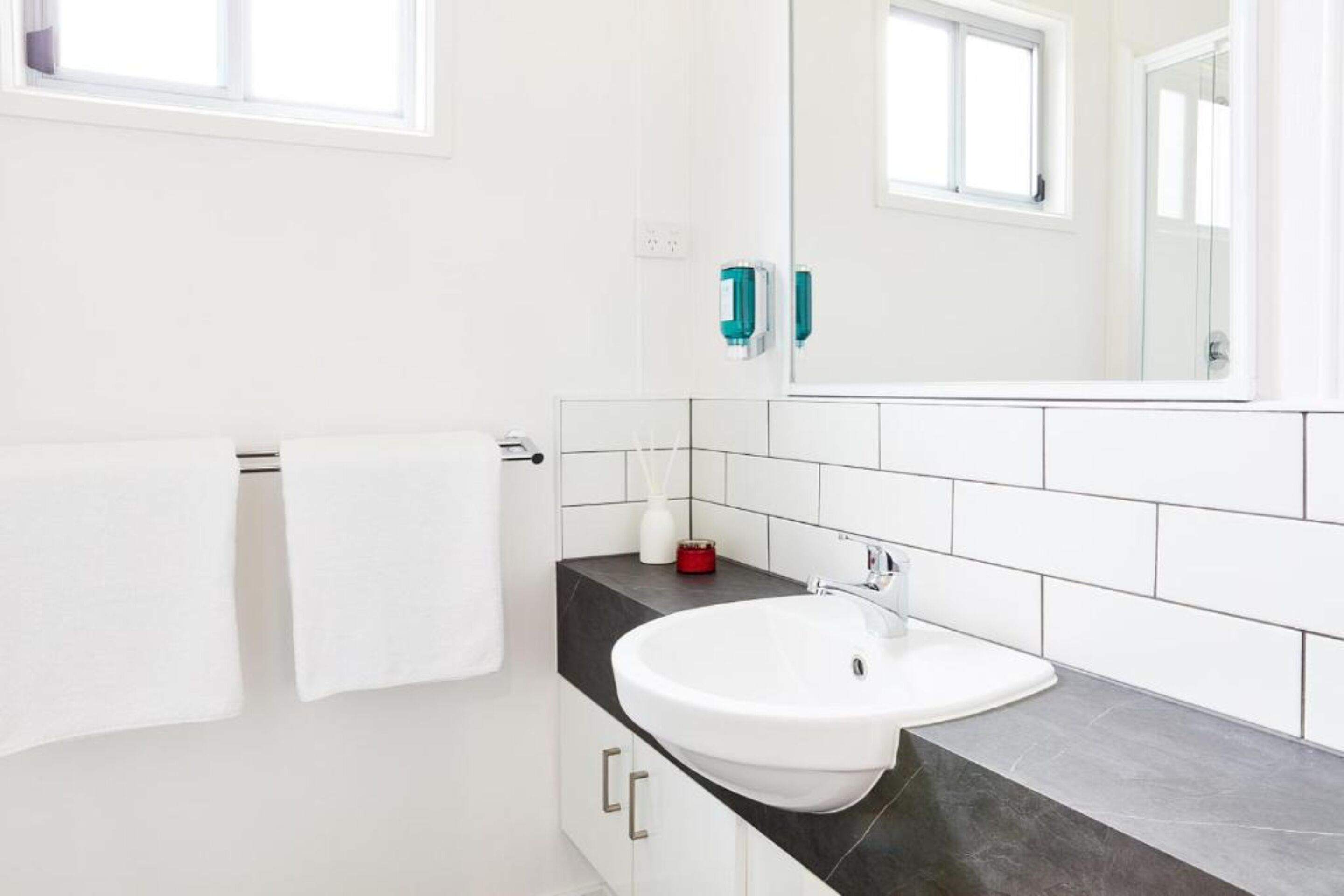 A modern bathroom with a white sink, dark countertop, and white tiled walls.