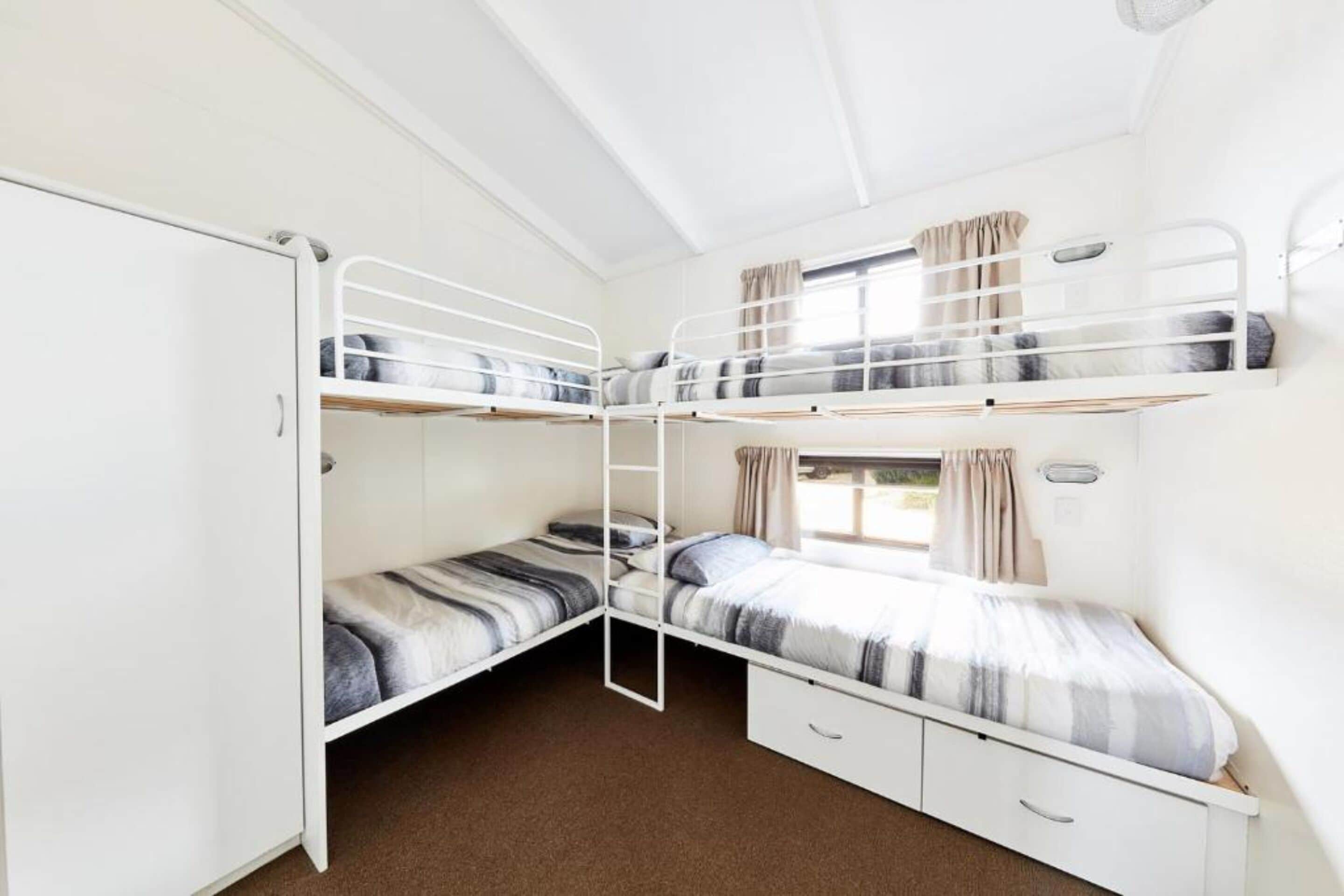 Habitación con literas, un armario blanco, una escalera y una ventana con cortinas.