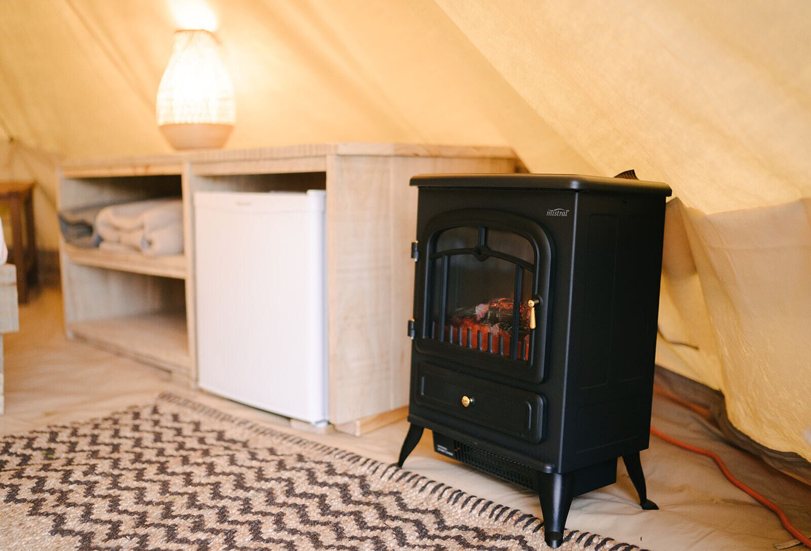 A compact black wood stove in a tented room with a white cabinet and a patterned rug.
