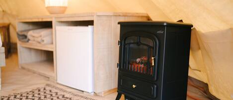 A compact black wood stove in a tented room with a white cabinet and a patterned rug.