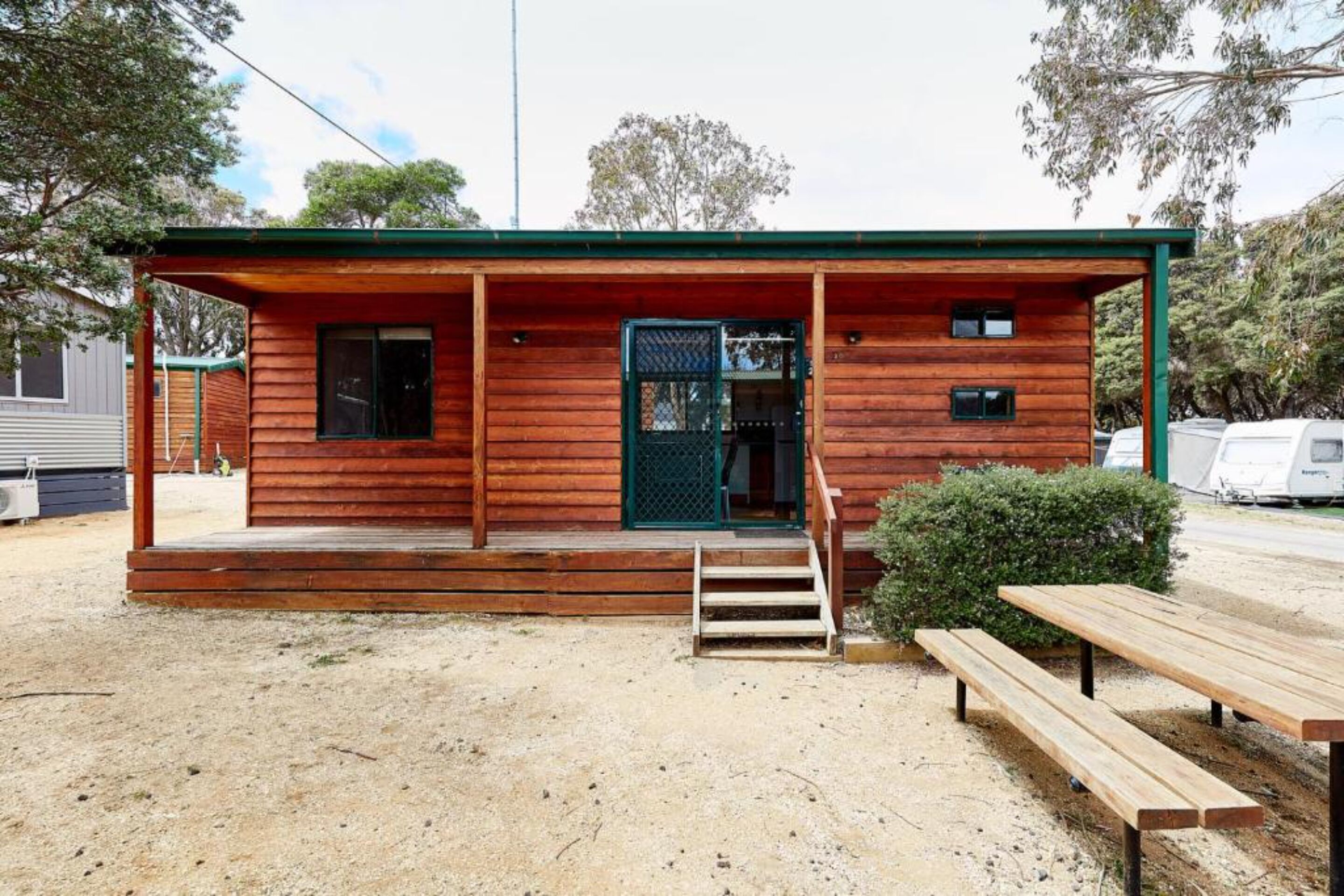 A wooden cabin with a porch, a green door, and a small window.