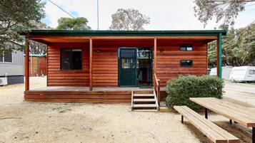 A wooden cabin with a porch, a green door, and a small window.