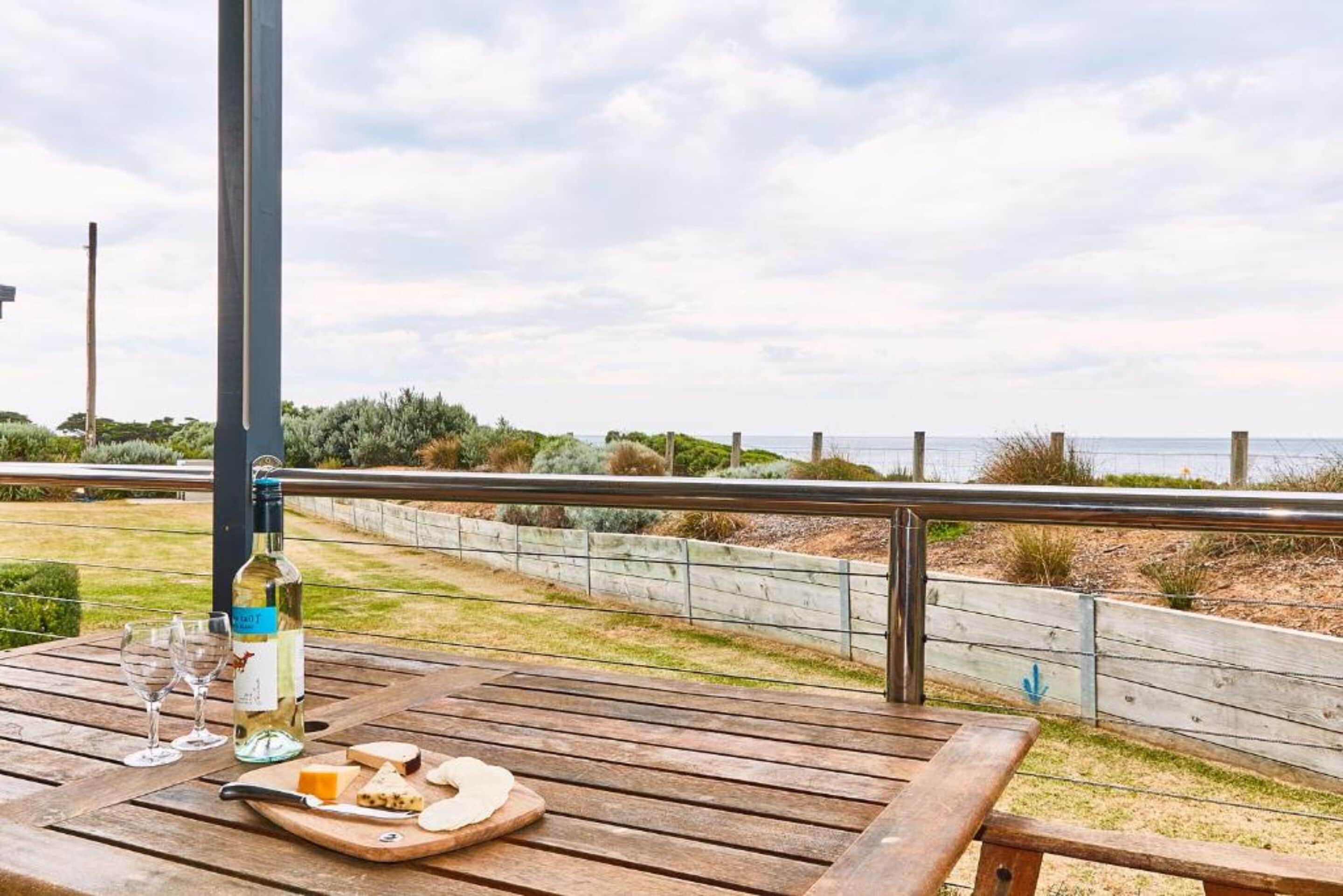A wooden deck with a bottle of white wine, glasses, and cheese on a wooden board.