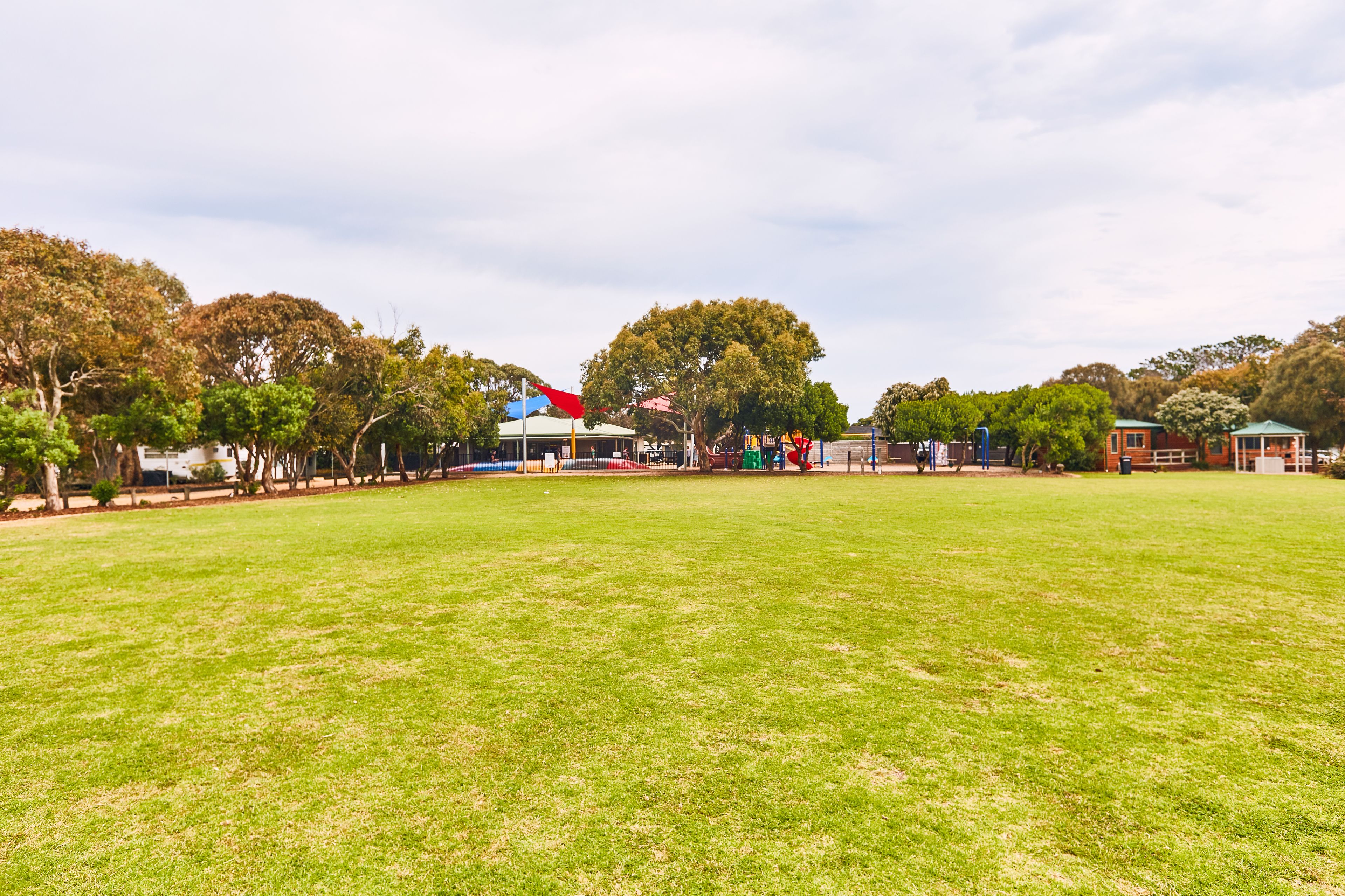 A grassy park area with trees, a playground, and a small building with a red roof.