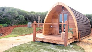 Una cabaña tipo A de madera con porche, una puerta y una ventana pequeña.