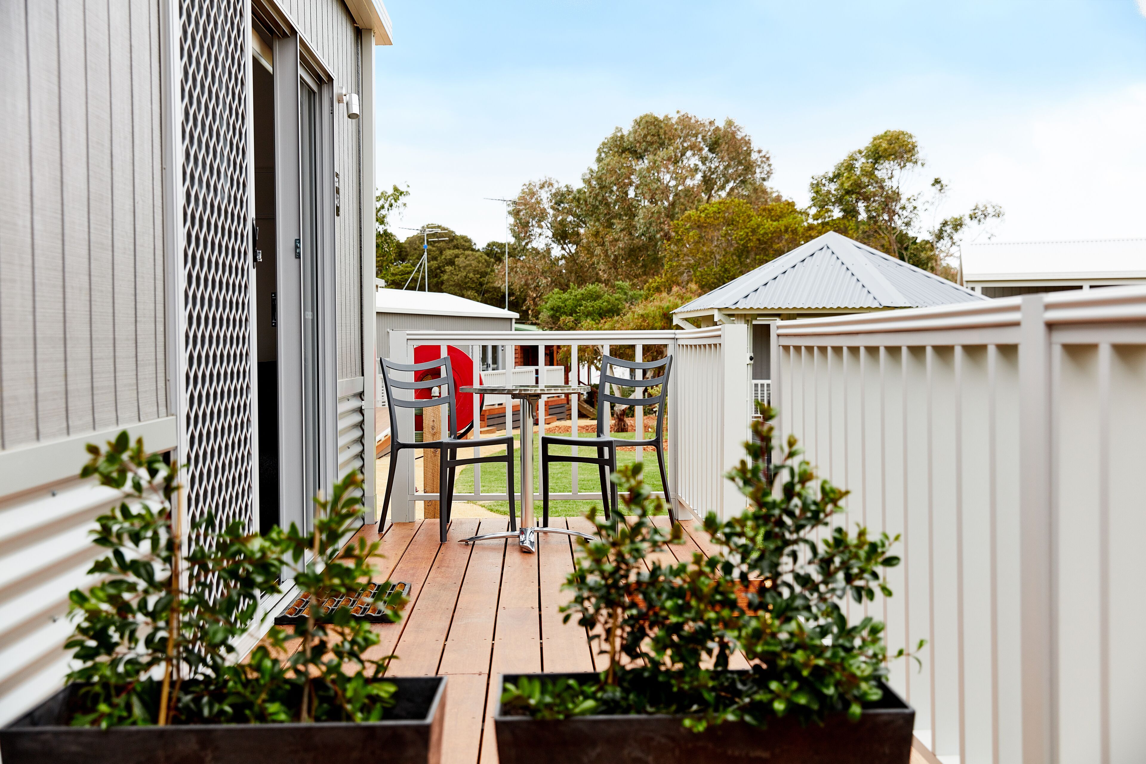 A wooden deck with a table and chairs, surrounded by white fences and potted plants.