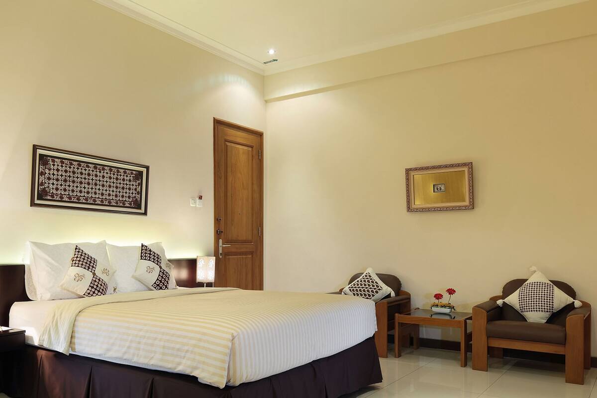 Une chambre d’hôtel avec un grand lit, des tables de chevet, une chaise, un bureau et une porte.