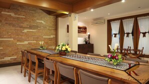 Un coin repas avec une longue table en bois, des chaises et un mur en briques. Un vase rempli de fleurs est posé sur la table.