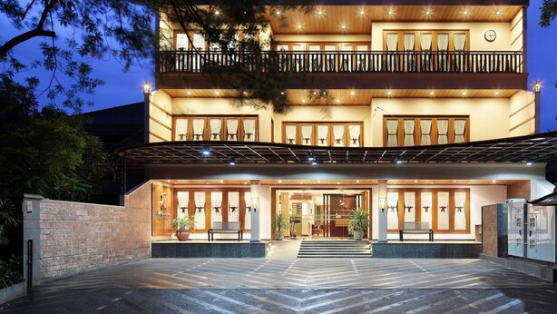 Un hôtel à plusieurs étages doté d’un balcon au deuxième étage, d’un hall d’accueil avec un banc et d’une grande entrée avec des marches.