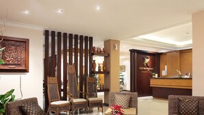 Un espace d’accueil d’hôtel avec un comptoir de réception en bois, plusieurs fauteuils en osier et un paravent décoratif en bois.