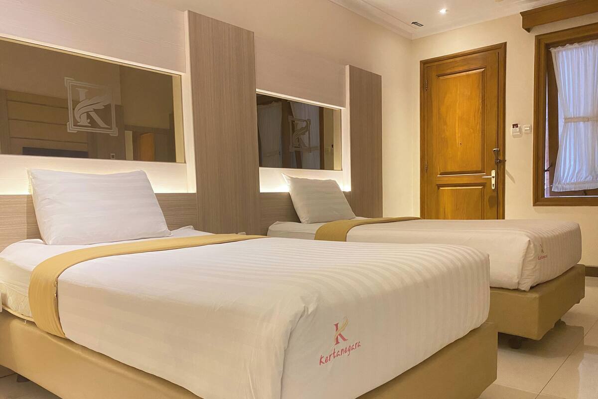 Une chambre d’hôtel avec deux lits, une porte en bois, une fenêtre avec des rideaux et un miroir au-dessus des lits.