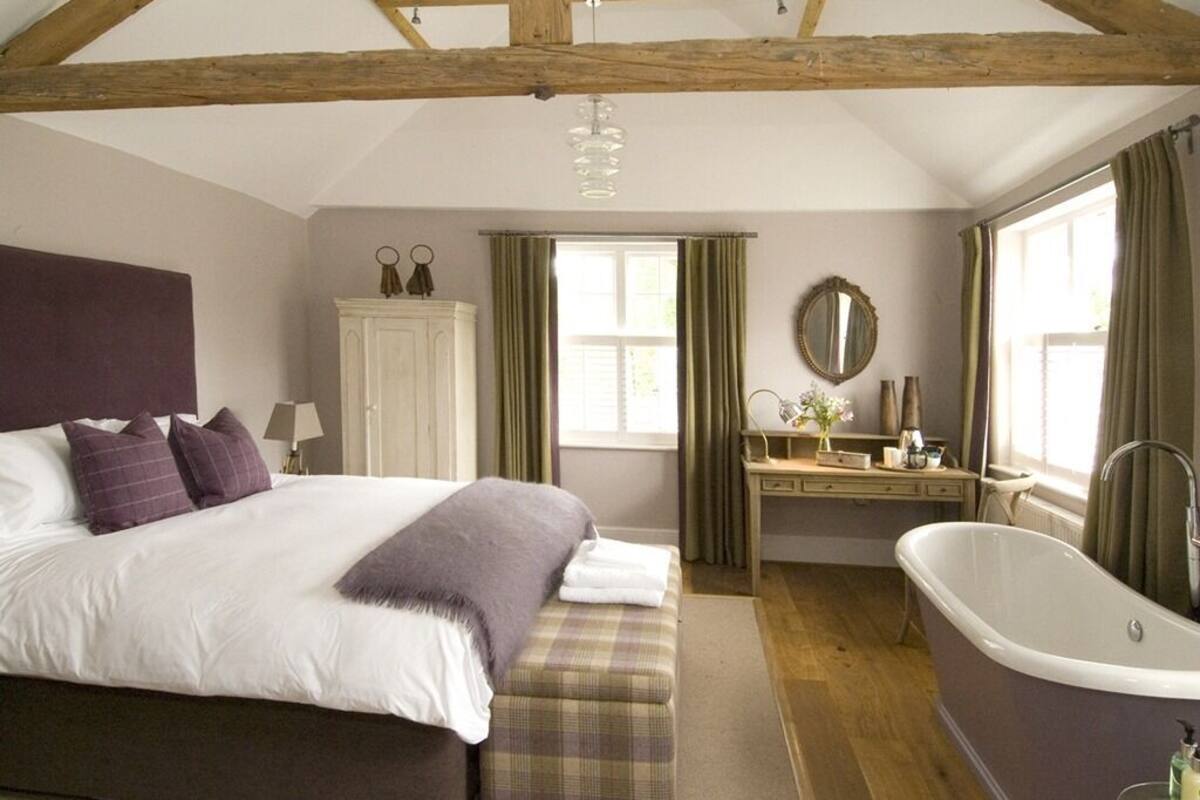 A bedroom with a large bed, a wooden ceiling, a vanity with a mirror, and a bathtub.