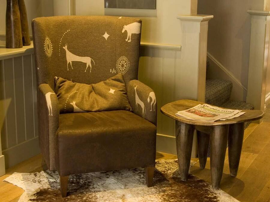 A chair with animal prints, a round wooden table with a newspaper, and a cowhide rug.