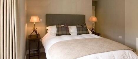 A neatly made bed with a headboard, two bedside lamps, and a window with curtains.
