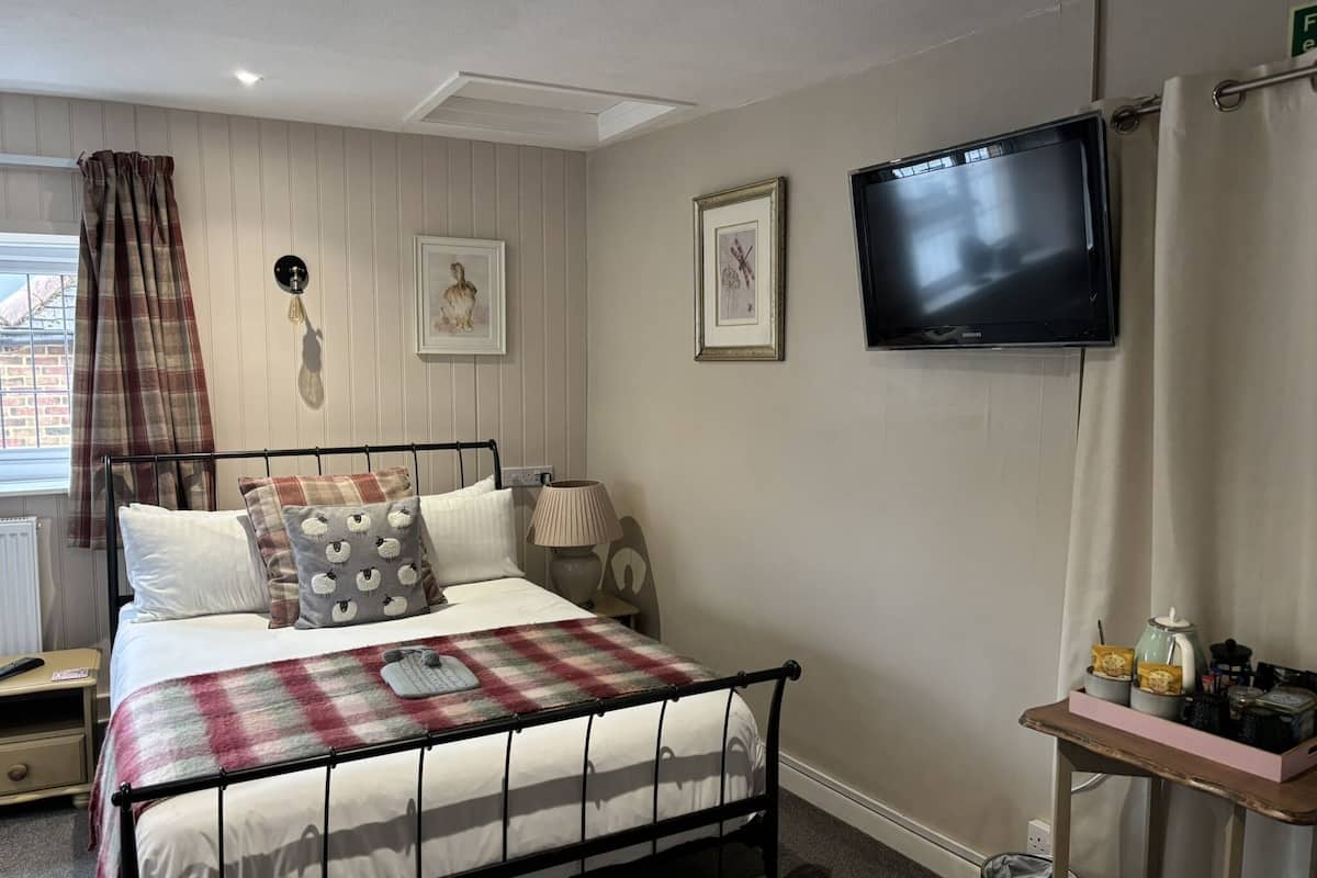 A bedroom with a bed, a television, a bedside table, and a window with curtains.