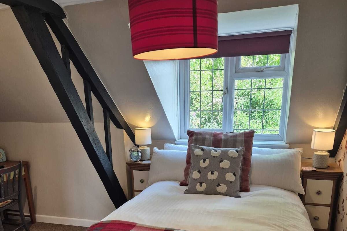 A bedroom with a bed, a window with a view, a red lamp, and a staircase.
