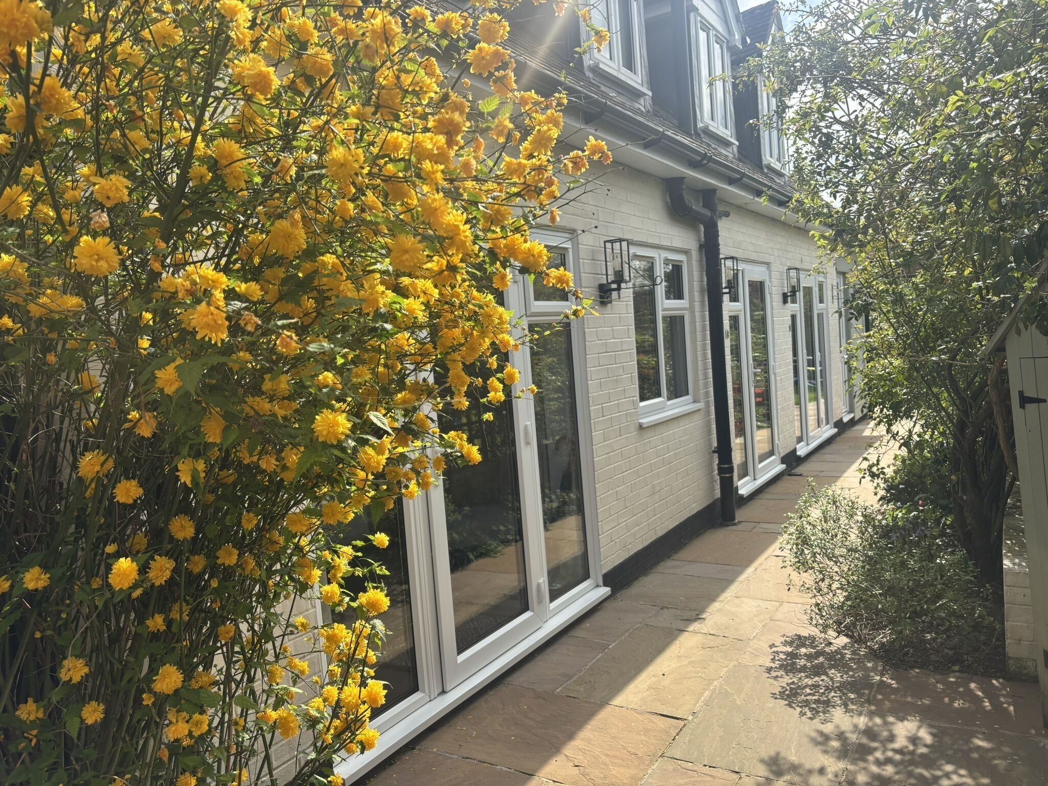 Une maison avec un chemin qui traverse le jardin, une façade en briques blanches et de grandes fenêtres.