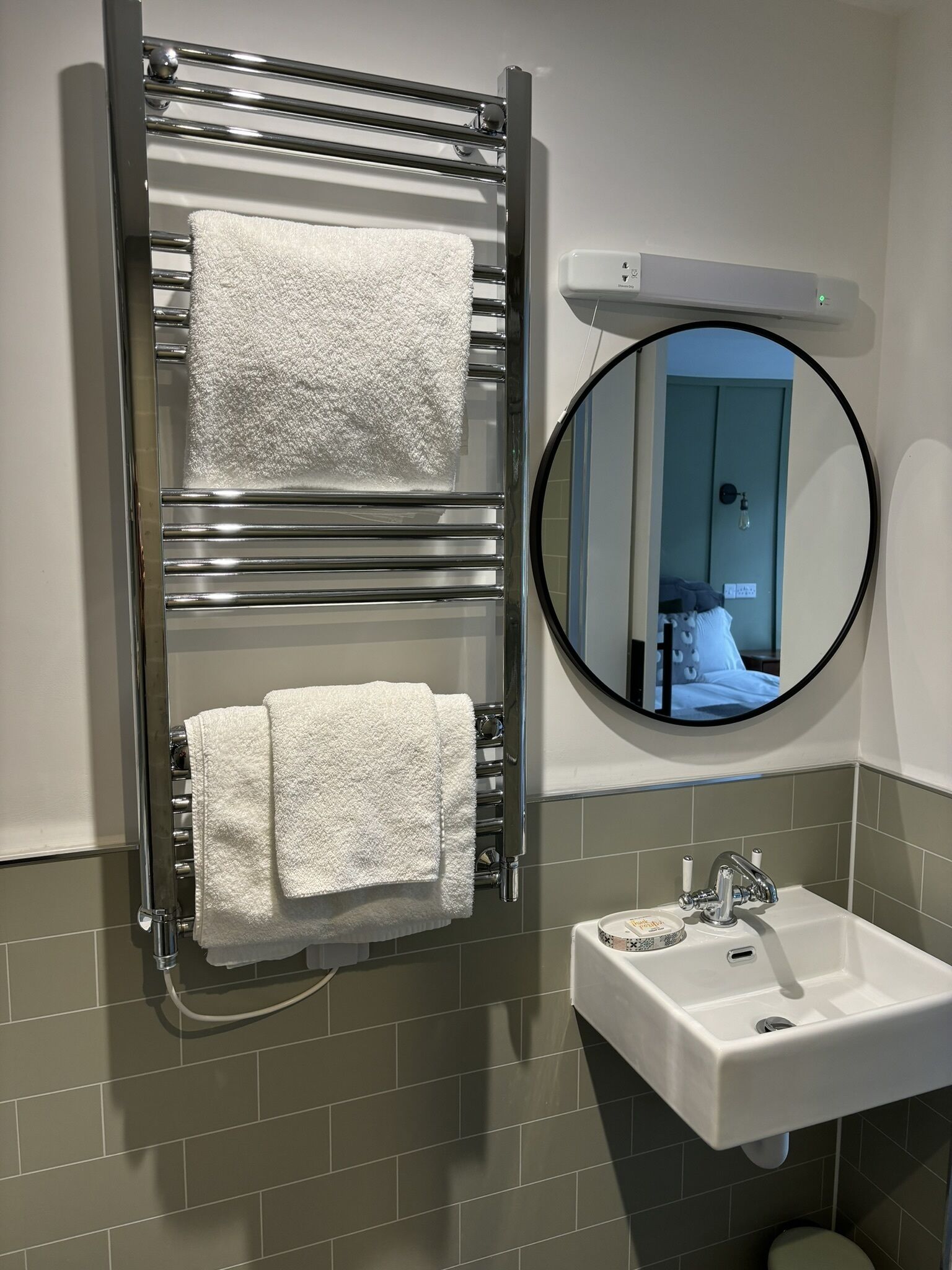 A bathroom with a chrome towel rack holding two white towels, a round mirror, and a white sink with a marble countertop.
