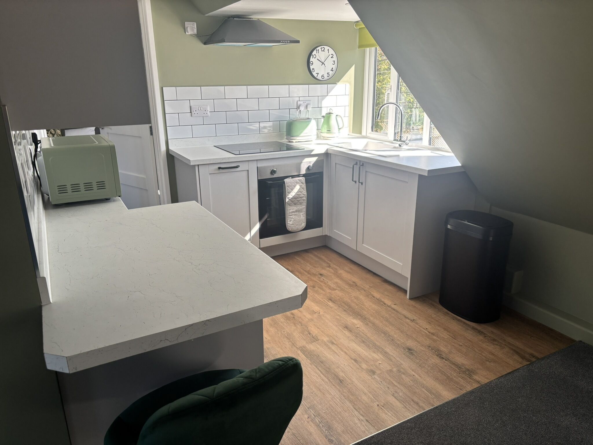 A kitchen with white cabinets, a tiled backsplash, a clock, and a window.