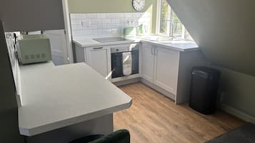 A kitchen with white cabinets, a tiled backsplash, a clock, and a window.