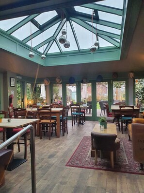 A restaurant with a glass ceiling, wooden tables and chairs, and a view of the outdoors.