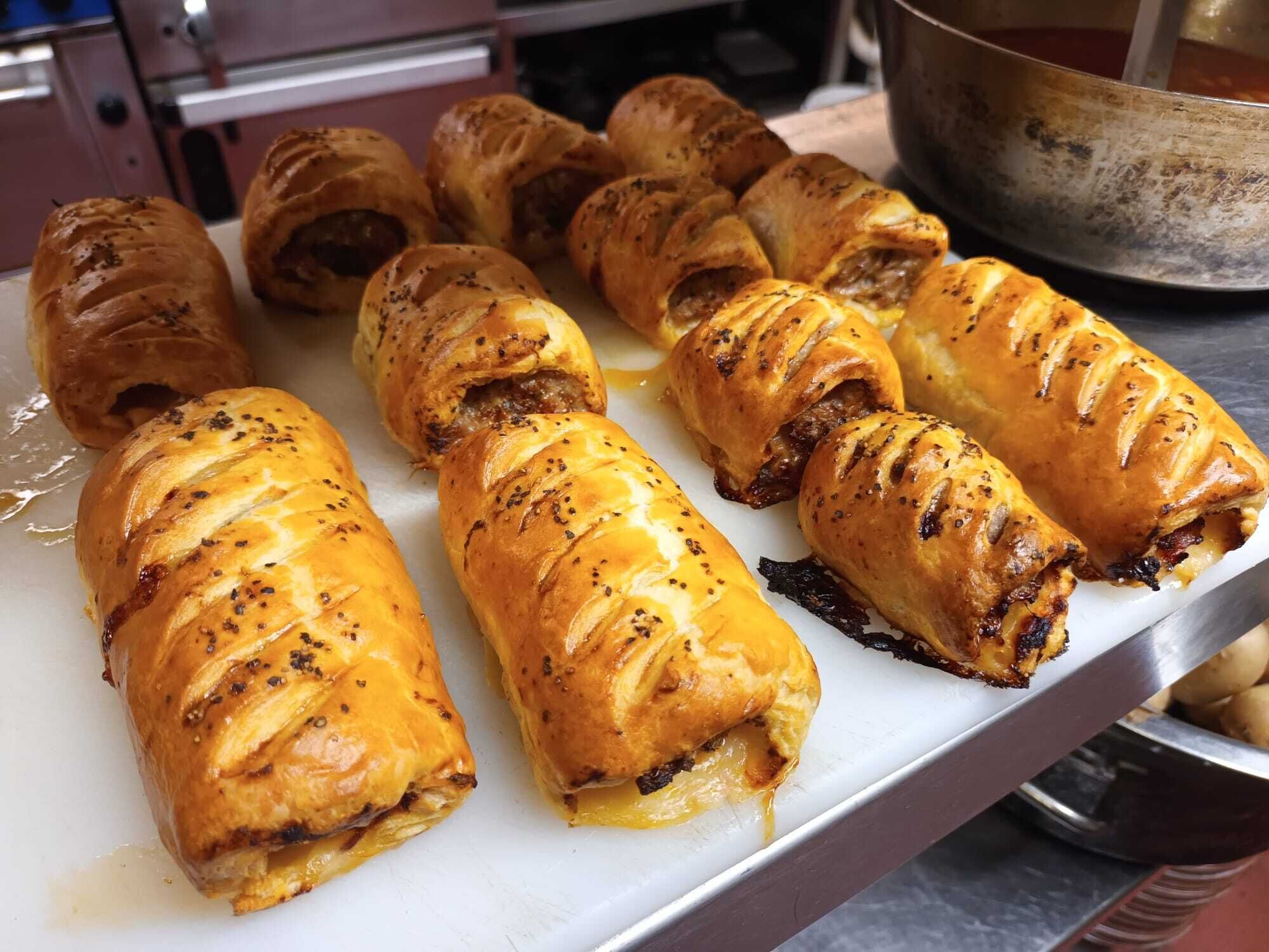 A tray of baked pastries with a golden-brown crust, possibly a type of bread or pastry, arranged on a white surface.