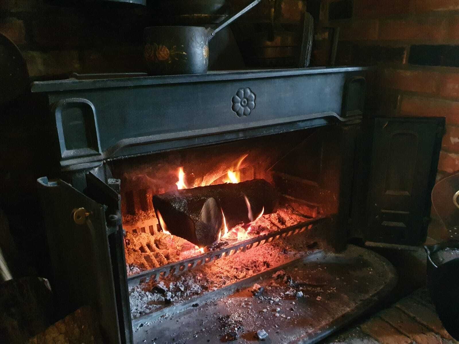 A wood-burning stove with a pot on top, a fire burning inside, and a metal grate below.
