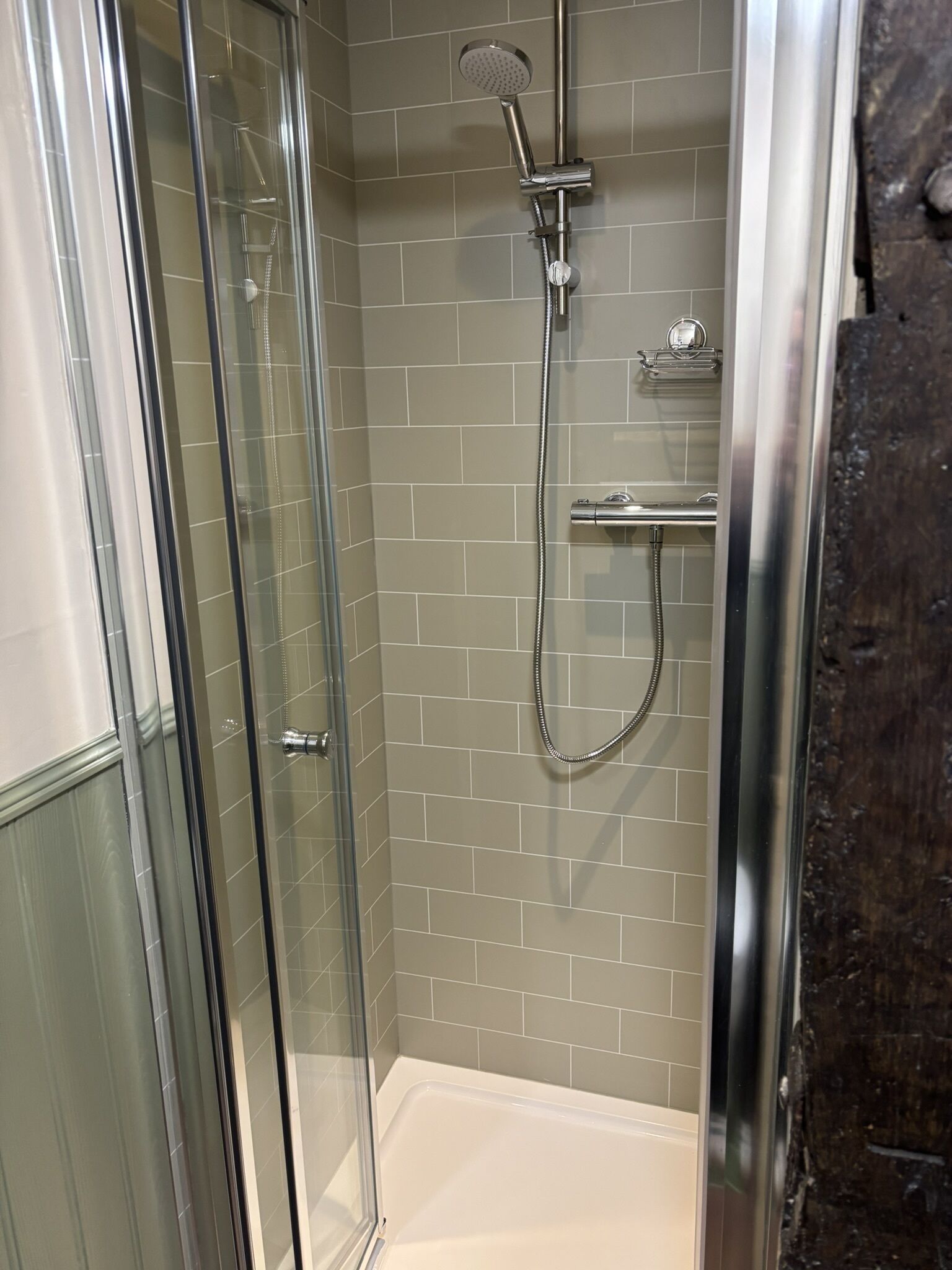 Une douche fermée par des parois en verre, dotée d’un pommeau de douche à main et d’un robinet mural.