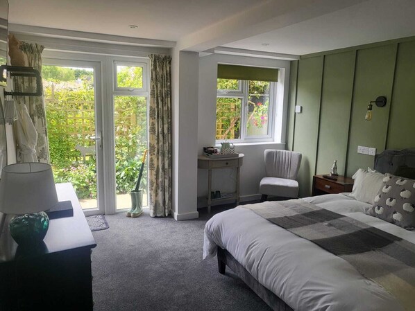 A bedroom with a large bed, a bedside table, a chair, and a window with a view of greenery.