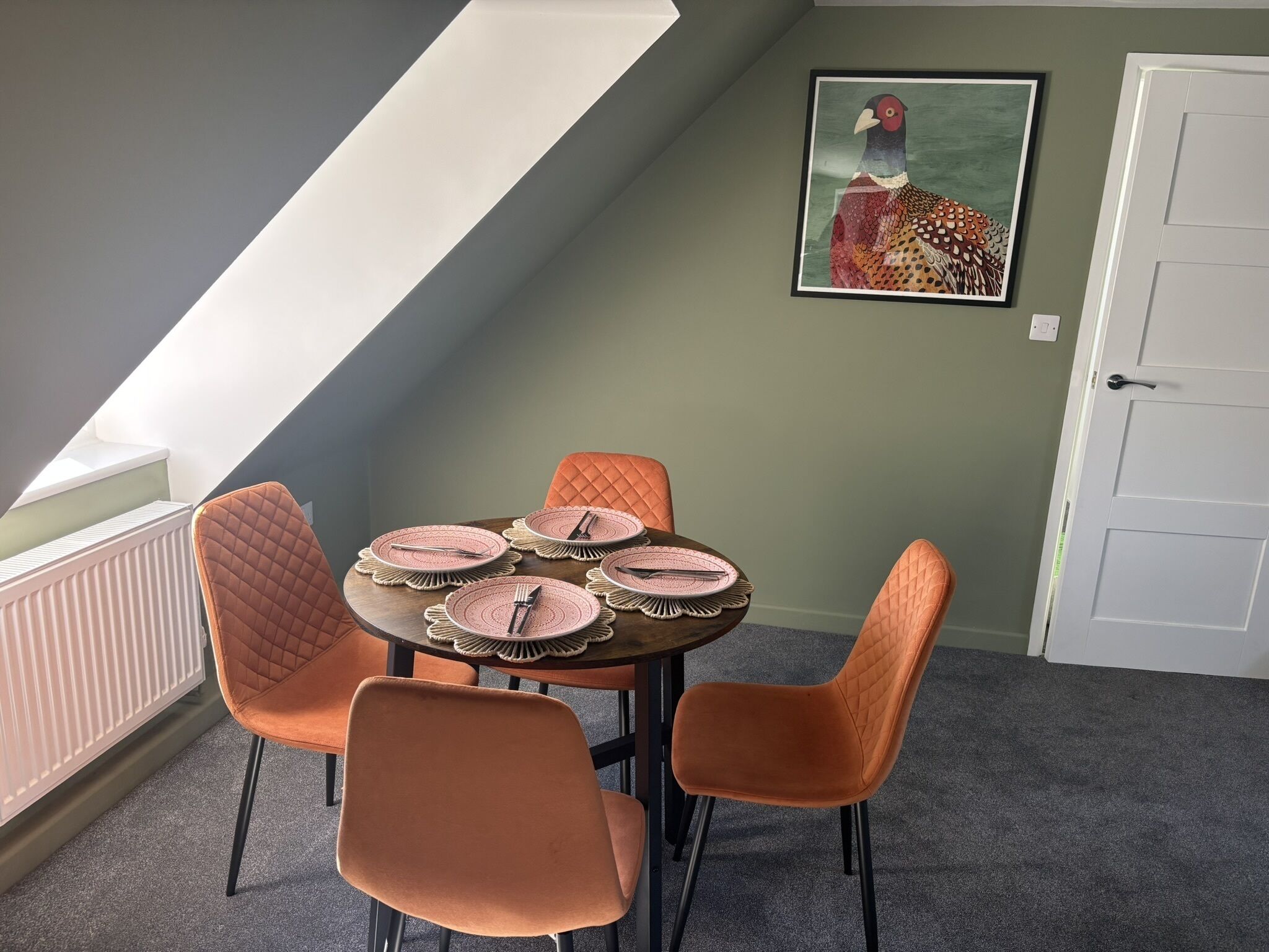 A dining area with a round table set for four, surrounded by four orange chairs.