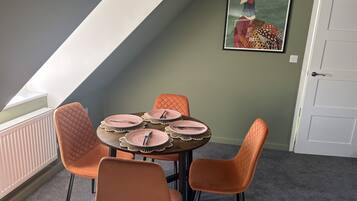 A dining area with a round table set for four, surrounded by four orange chairs.
